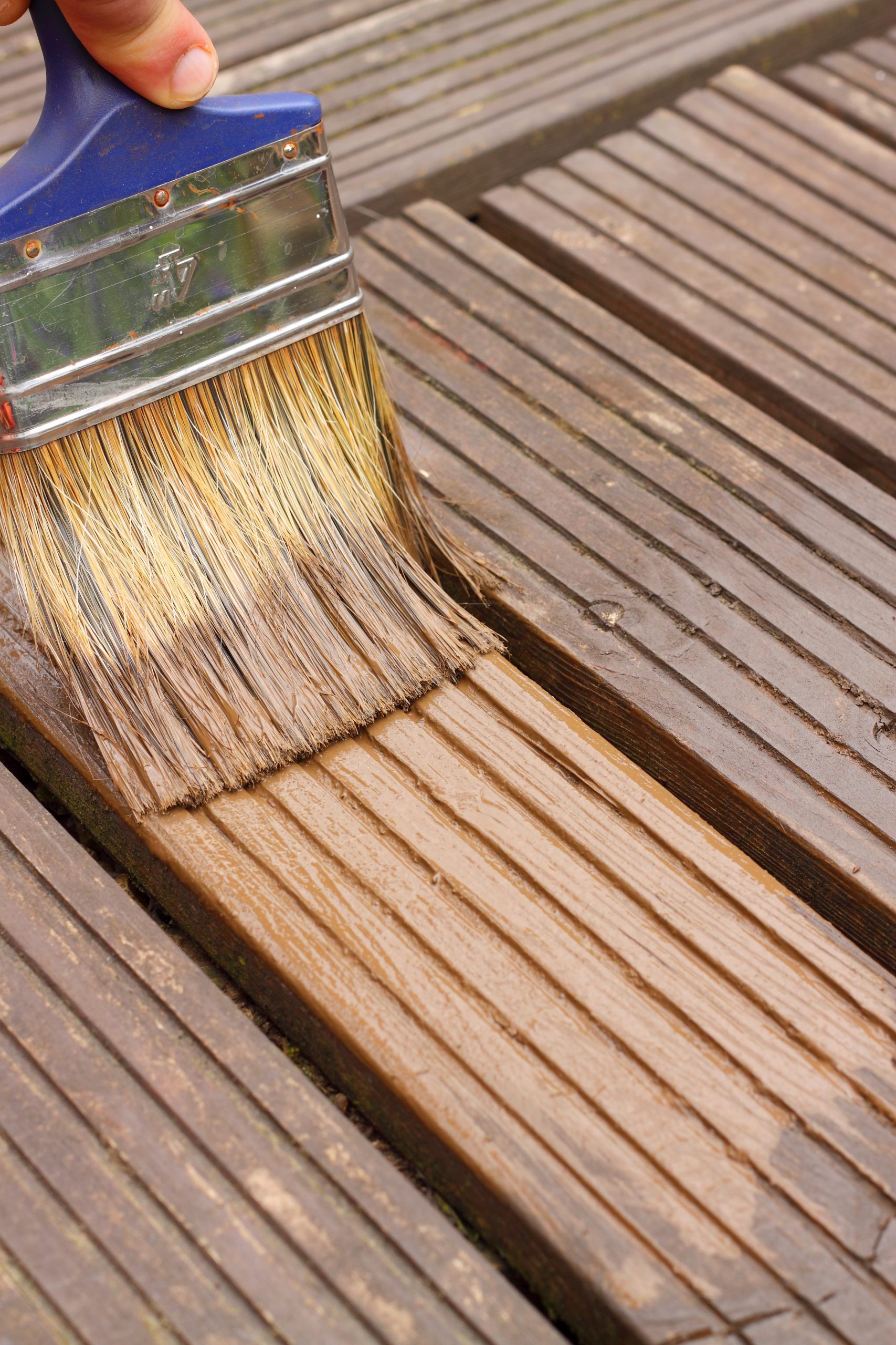 Paint brush applying stain to deck